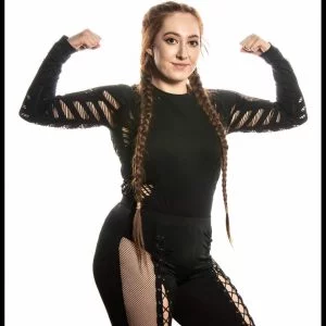 Evelyn stands posed flexing biceps in a black partly netting outfit with hair in long braids.
