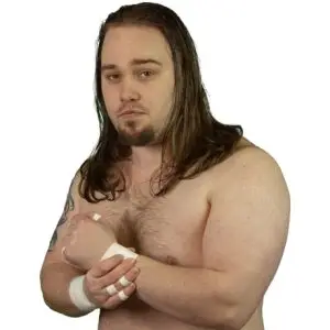 Sean Dymond a wrestler with long shoulder length brown hair and a goatee beard stands holding his wrist which have tape on as well as some of his fingers