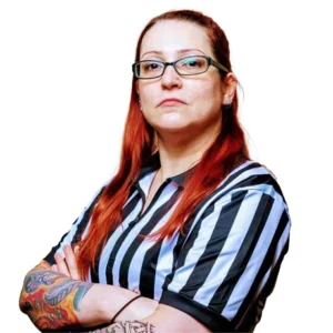 Lilith stands arms folded in her referee's shirt with glasses red hair and tattoos