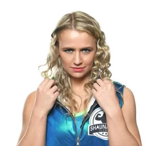 Shuna is wearing an iridescent blue top and has blonde curly hair