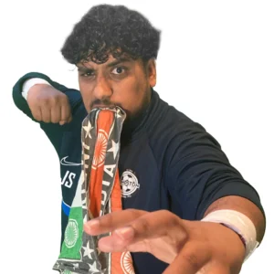 Shogun J stands posed at the camera with white wrist tape a black t-shirt and in his mouth he has a towel covered in India flags