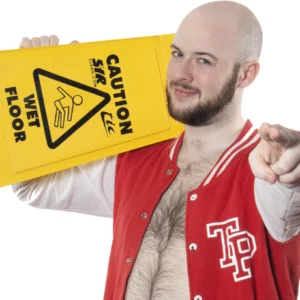 Theodore wears a red baseball style jacket with is initials on as he points to camera holding a wet floor sign.